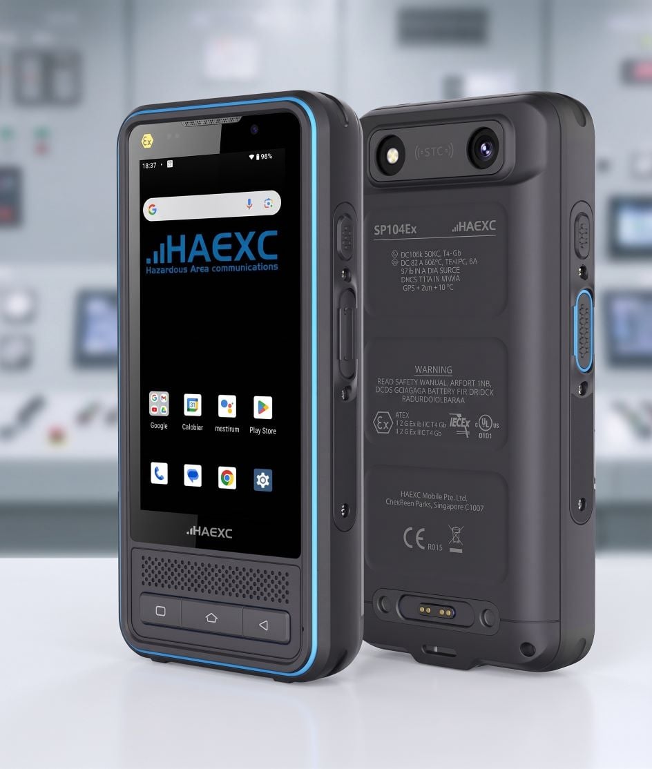 Front and back view of the HAEXC SP104Ex intrinsically safe smartphone, featuring a rugged black body with blue accent trim, physical navigation buttons, and hazardous-area safety markings against a blurred control room background