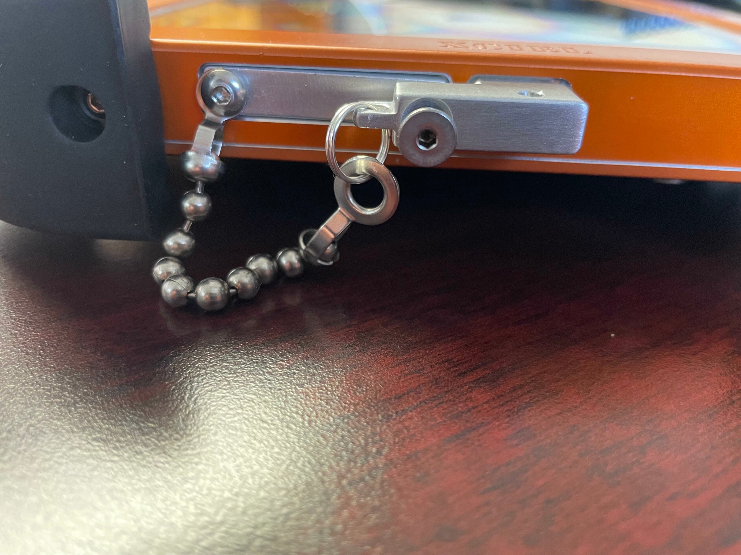 Close-up of the Atexxo explosion-proof iPad Mini aluminum casing featuring a flameproof metal charging slot cover secured with a hex screw and tethered stainless steel safety ball chain.